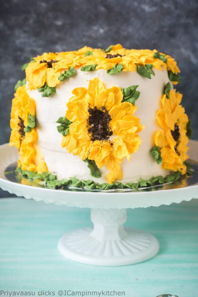 Whole wheat carrot pineapple cake on cake stand with sunflower design buttercream